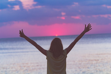 Woman with arms wide open looking at the sunset over ocean / sea.