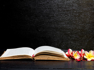 Book and frangipani flowers isolated black background on wooden table