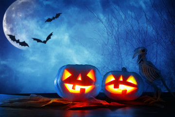 Halloween holiday concept. Pumpkins over wooden table at night scary, haunted and misty forest.