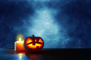 Halloween holiday concept. Pumpkins over wooden table at night scary, haunted and misty forest.