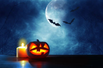 Halloween holiday concept. Pumpkins over wooden table at night scary, haunted and misty forest.