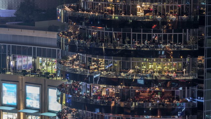 Aerial vew of Dubai Marina promenade with restaurants from skyscraper night timelapse, United Arab Emirates.