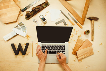 male hands typing on laptop on carpentry work tools background with wooden cuttings.