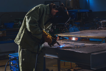 concentrated manufacture worker welding metal with sparks at factory