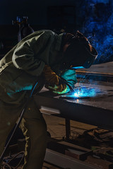 male manufacture worker welding metal with sparks at factory