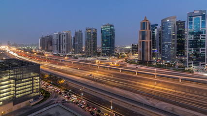 Aerial view of Jumeirah lakes towers skyscrapers day to night timelapse with traffic on sheikh zayed road.
