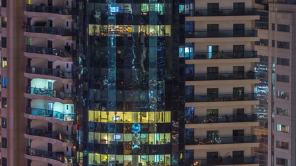 Fototapeta na wymiar Windows of the multi-storey building of glass and steel lighting inside and moving people within timelapse