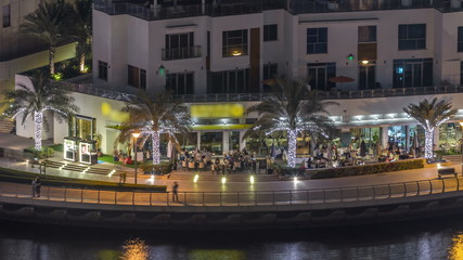Promenade and canal in Dubai Marina with luxury skyscrapers and yachts around night timelapse, United Arab Emirates