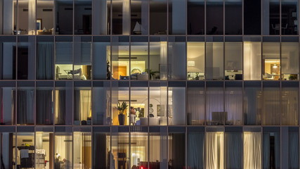 Windows of the multi-storey building of glass and steel lighting inside and moving people within timelapse