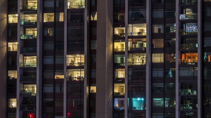 Windows of the multi-storey building of glass and steel lighting inside and moving people within timelapse