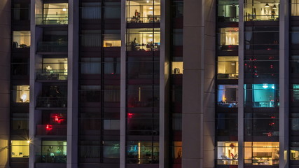 Windows of the multi-storey building of glass and steel lighting inside and moving people within timelapse