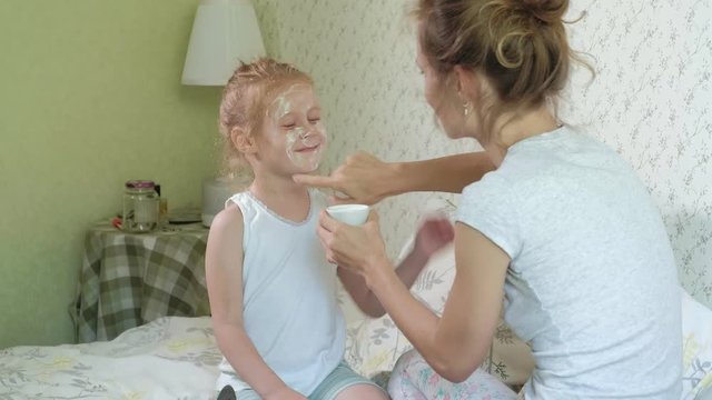 A woman with her daughter makes fun of cucumber masks at home