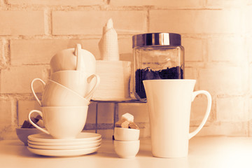 Tea drink concept. Piece of cafe, restaurant interior with teapot, tea cups, sugar cubes, tea leaves, paper napkins, saucers on white board against white brick wall.