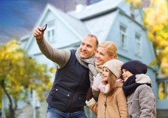 Fototapeta premium family, technology and real estate concept - happy mother, father, daughter and son taking selfie by smartphone over living house background outdoors in autumn