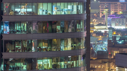 Windows of the multi-storey building of glass and steel lighting inside and moving people within timelapse