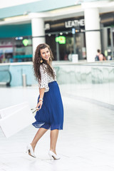 beautiful stylish girl holding paper bags and smiling at camera in shopping mall