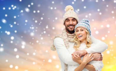 winter, christmas and people concept - smiling couple in hats and knitwear hugging over snow background