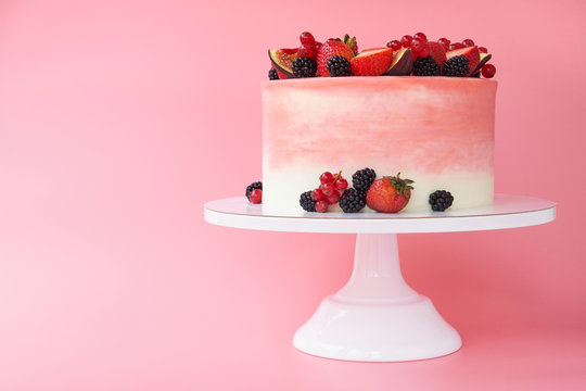Cake with whipped pink cream, decorated with fresh strawberries, blackberry, figs and red currant on pink background. Picture for a menu or a confectionery catalog.
