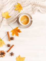 Obraz na płótnie Canvas Autumn or winter cozy composition. Cup of coffee, warm knitted plaid, cinnamon sticks, anise star and dry leaves on a white background wooden table. Flat lay, top view, copy space 
