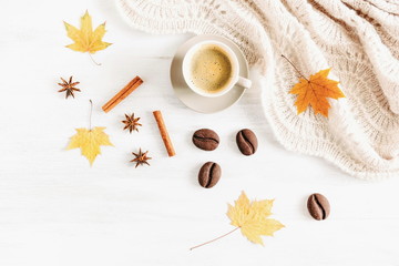 Autumn or winter cozy composition. Cup of coffee, warm knitted plaid, chocolate cookies, cinnamon sticks, aniseed star and dry leaves on a white background. Flat lay, top view, copy space 