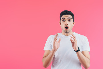 shocked handsome man gesturing and looking at camera isolated on pink