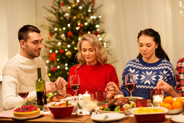 holidays and celebration concept - friends holding hands and praying before christmas dinner at home