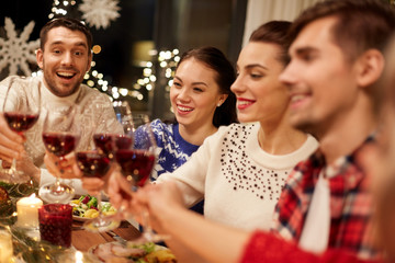 holidays and celebration concept - happy friends having christmas dinner at home, drinking red wine and clinking glasses