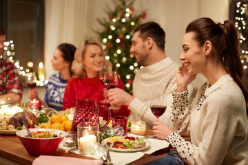 holidays, communication and celebration concept - happy young woman calling on smartphone and having christmas dinner with friends at home