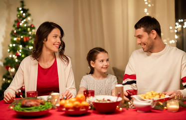 holidays, family and celebration concept - happy mother, father and little daughter having christmas dinner at home