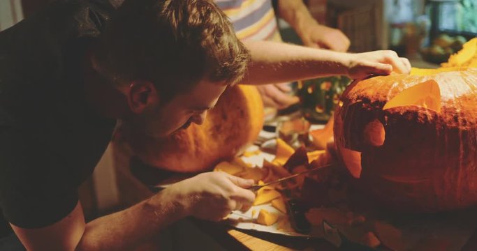 Man Carves Pumpkin for Halloween Celebration. 4K SLOW MOTION. Young man cutting details of a Jack O' Lantern pumpkin decoration at home. Autumn aesthetics. 