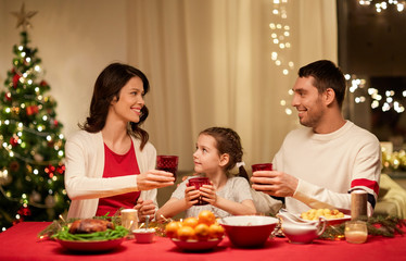 holidays, family and celebration concept - happy mother, father and little daughter having christmas dinner at home