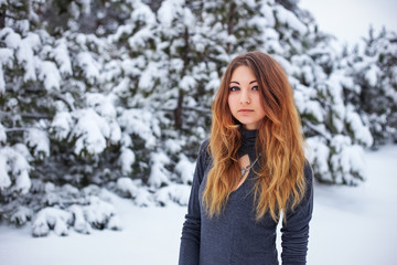 Beautiful young girl posing in the winter in cold forest with pine trees.