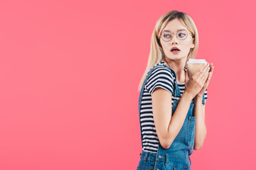 side view of shocked young woman with coffee to go isolated on pink
