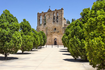 Fototapeta na wymiar Spain, Catalonia, Peratallada: Panorama front view of famous Sant Esteve church of small fortified medieval Spanish town with cross, facade, entrance, green trees, beautiful stone street and blue sky.