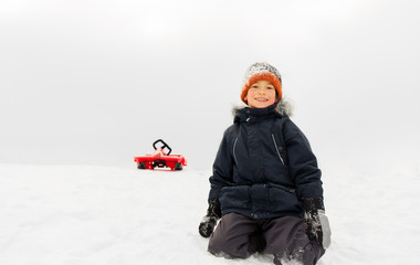 Fototapeta na wymiar childhood, sledging and season concept - happy little boy and sled down snow hill outdoors in winter