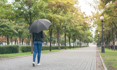 girl in a black leather jacket and blue jeans with a black umbrella in her hands on the mall
