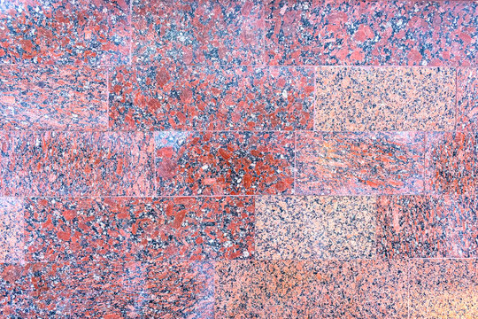 Red granite tiles pattern with a relief structure, background. The texture of solid granite tiles. Hard and slippery red granite surface with a relief discharge. Polished granite wall