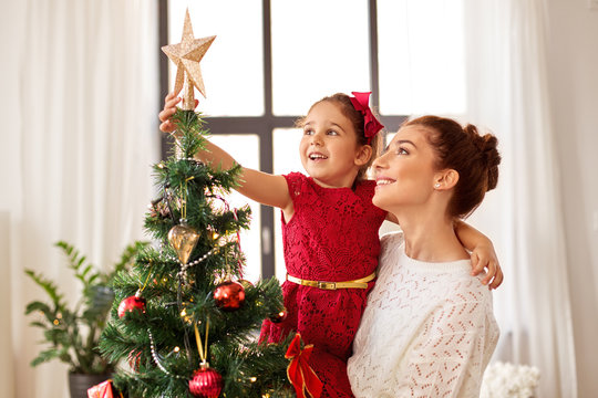 family, winter holidays and people concept - happy mother and little daughter decorating christmas tree at home