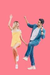 happy young couple looking at each other and dancing isolated on pink