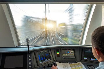 Train driver at the controls cab of speed passenger train, view of the railway bridge with the...