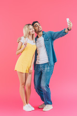 handsome young man taking selfie with girlfriend doing peace sign on smartphone isolated on pink