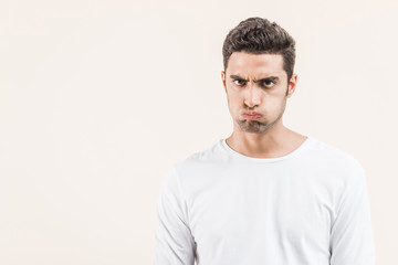 Fototapeta premium angry young man blowing cheeks and looking at camera isolated on beige