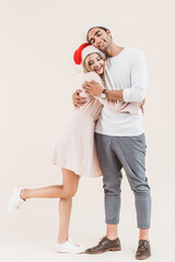 Obraz premium happy young couple in santa hats hugging isolated on beige