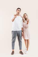 aggressive young couple giving the fingers and looking at camera isolated on beige