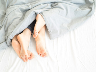 Couple on white bed in hotel room focus at feet.