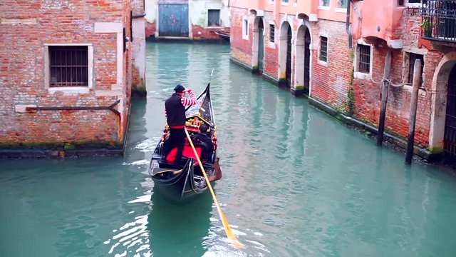 Gondolier navigates the gondola occupied with tourists through the narrow canal in Venice Italy during winter