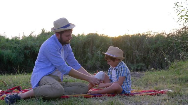 dad puts a tight bandage on the injured knee of the son sitting on the rug during a family weekend at countryside