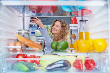 Woman taking food from fridge full of groceries. Picture taken from the inside of fridge.
