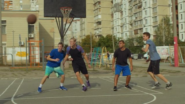 Handsome teenage basketball player completing offense with jump shot and scoring points while playing streetball game on outdoor court. Young streetball player taking jump shot to score points outdoor