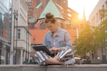 Young woman in in a denim jacket sitting and typing on laptop in Lubeck city. Germany